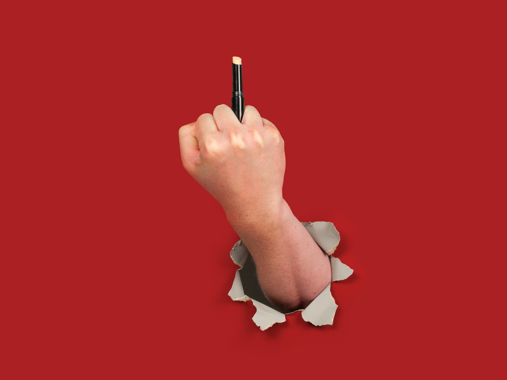Hands breaking through red paper wall holding the concealer product as if it were the middle finger